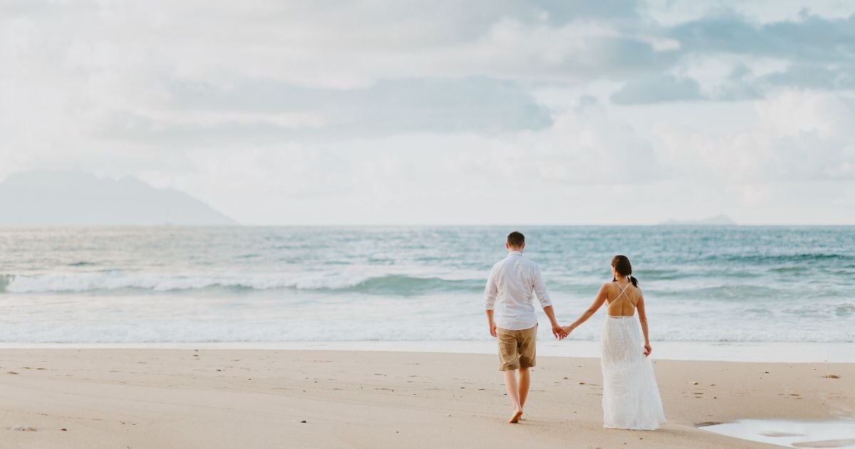 bride and groom holding hands walking on the beach 